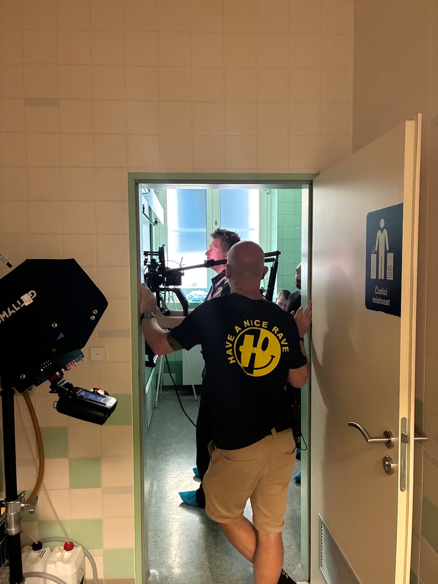 Crew filming through a doorway in a tiled hospital corridor